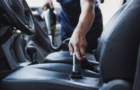 cropped view of car cleaner vacuuming drivers seat in car