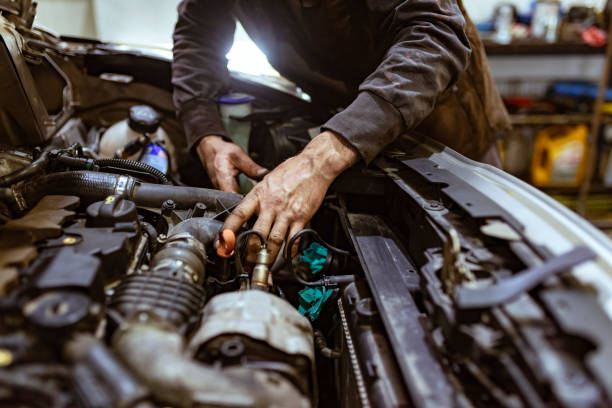 Young dirty mechanic working in a car repair shop. Auto mechanic working on car engine in mechanics garage. Repair service. authentic close-up shot. Photo of dirty car mechanic hands examining car automobile at a repair service station.